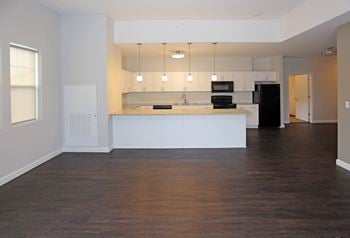 Open floor plan living room and kitchen with large breakfast bar, white cabinets, and black appliances.